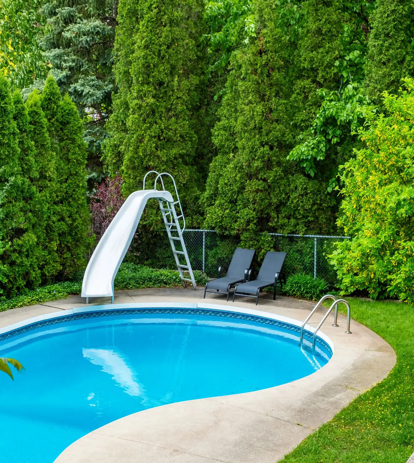 Here's an 8-word alt tag for the image: Blue kidney pool with slide and lounge chairs.