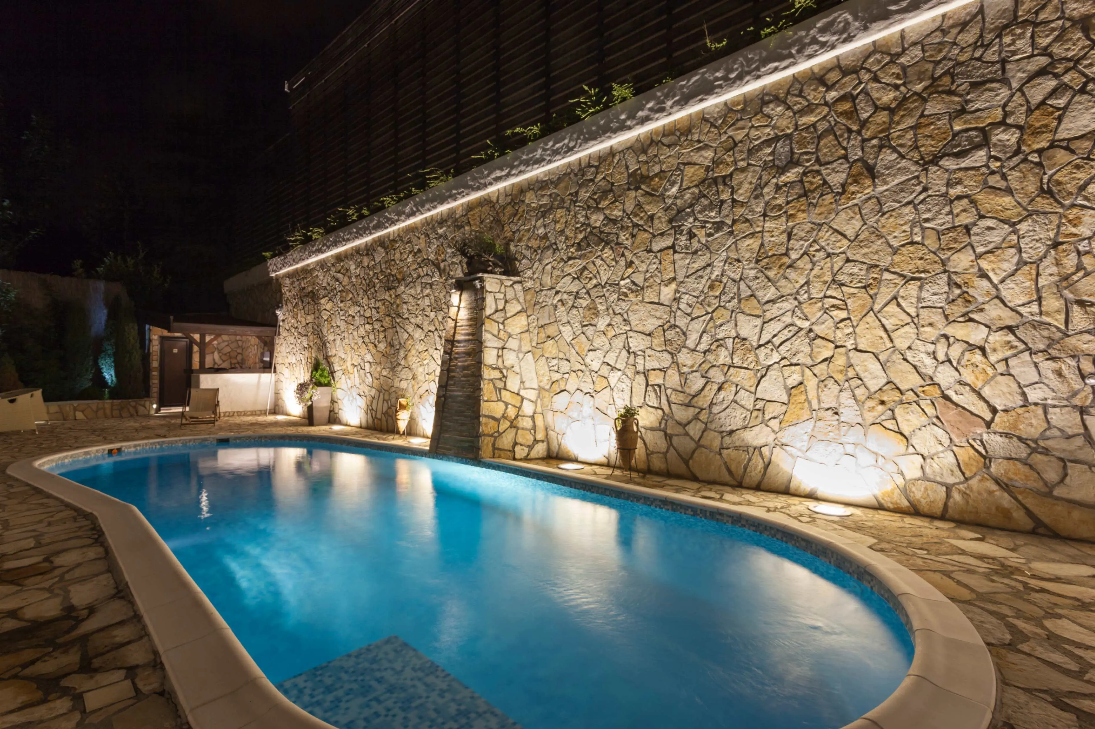 Night view of illuminated pool and stone wall.